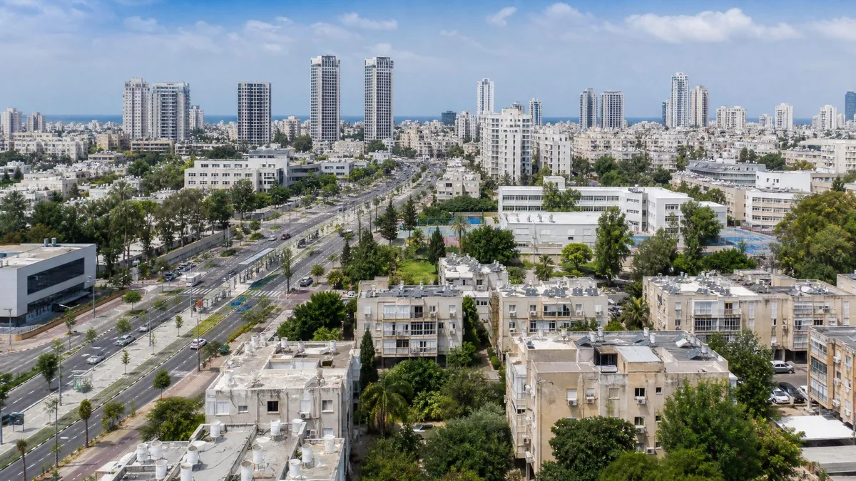 מבט עירוני רחב עם בנייה ותיקה, מגדלים חדשים וציר תנועה מרכזי לבחירת עיר להתחדשות עירונית